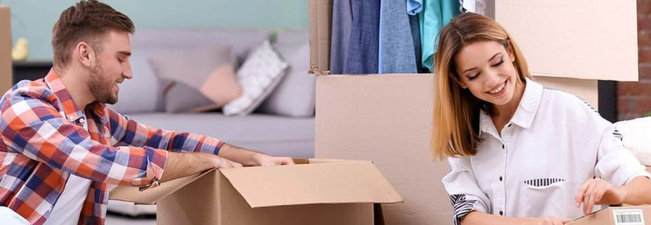 Smiling couple unpacking moving boxes in their new home with clothes and furniture in the background.
