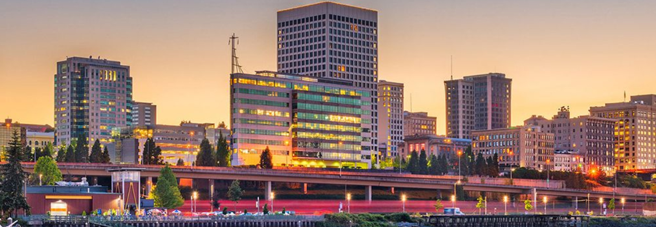 Tacoma city skyline at sunset with illuminated buildings and a waterfront view. Let me know if you need an alt text related to Move Northwest Moving & Storage!