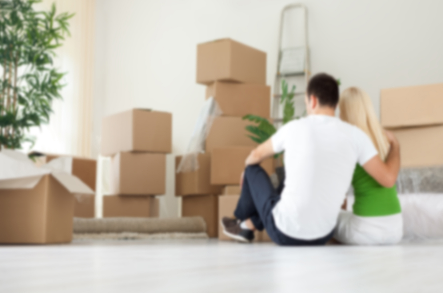 Couple sitting on the floor embracing, surrounded by Moving Boxes in their new home.