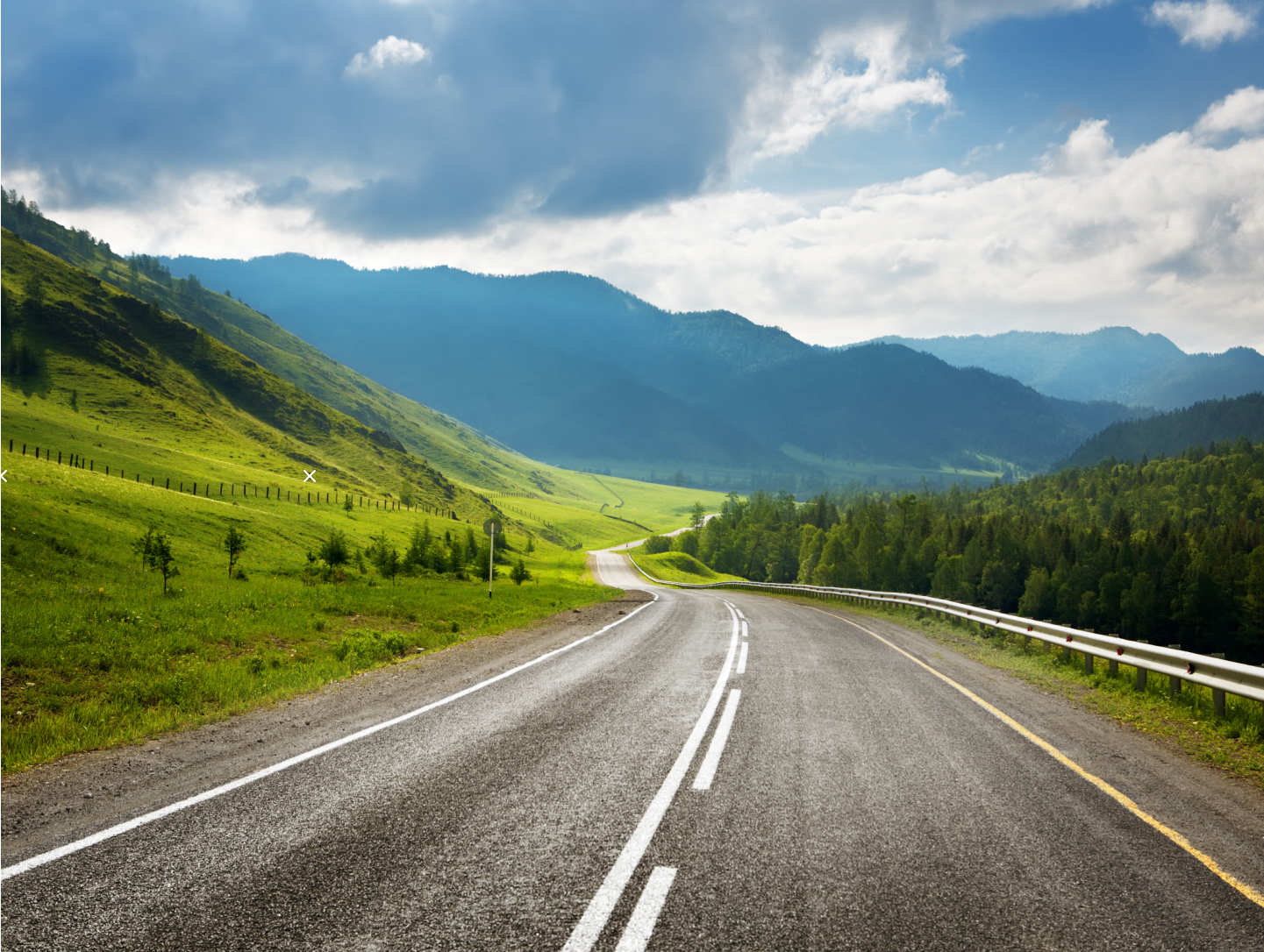 Scenic winding road through lush green hills and mountains under a partly cloudy sky.