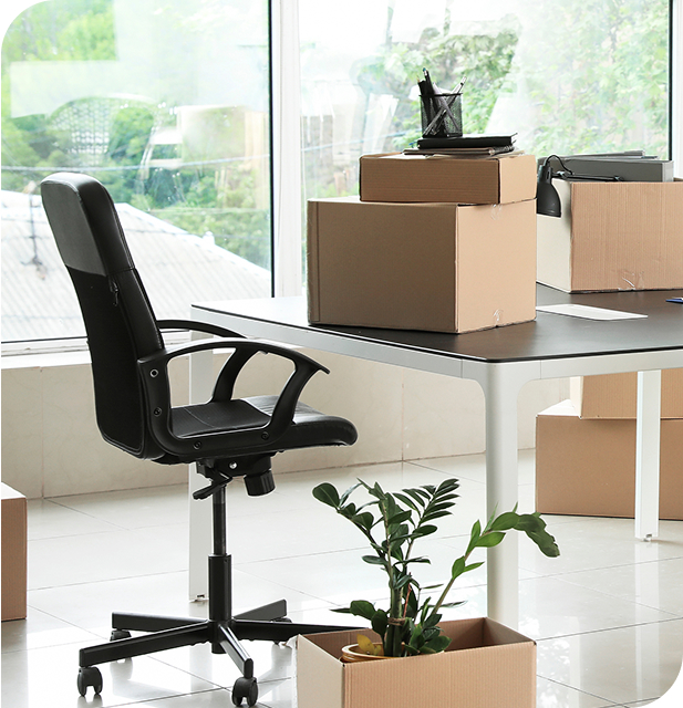 Office space with Moving Boxes stacked on a desk and a black chair near a large window.