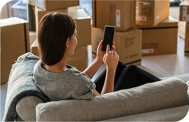 Woman sitting on a couch using her phone, surrounded by Moving Boxes in a new home.